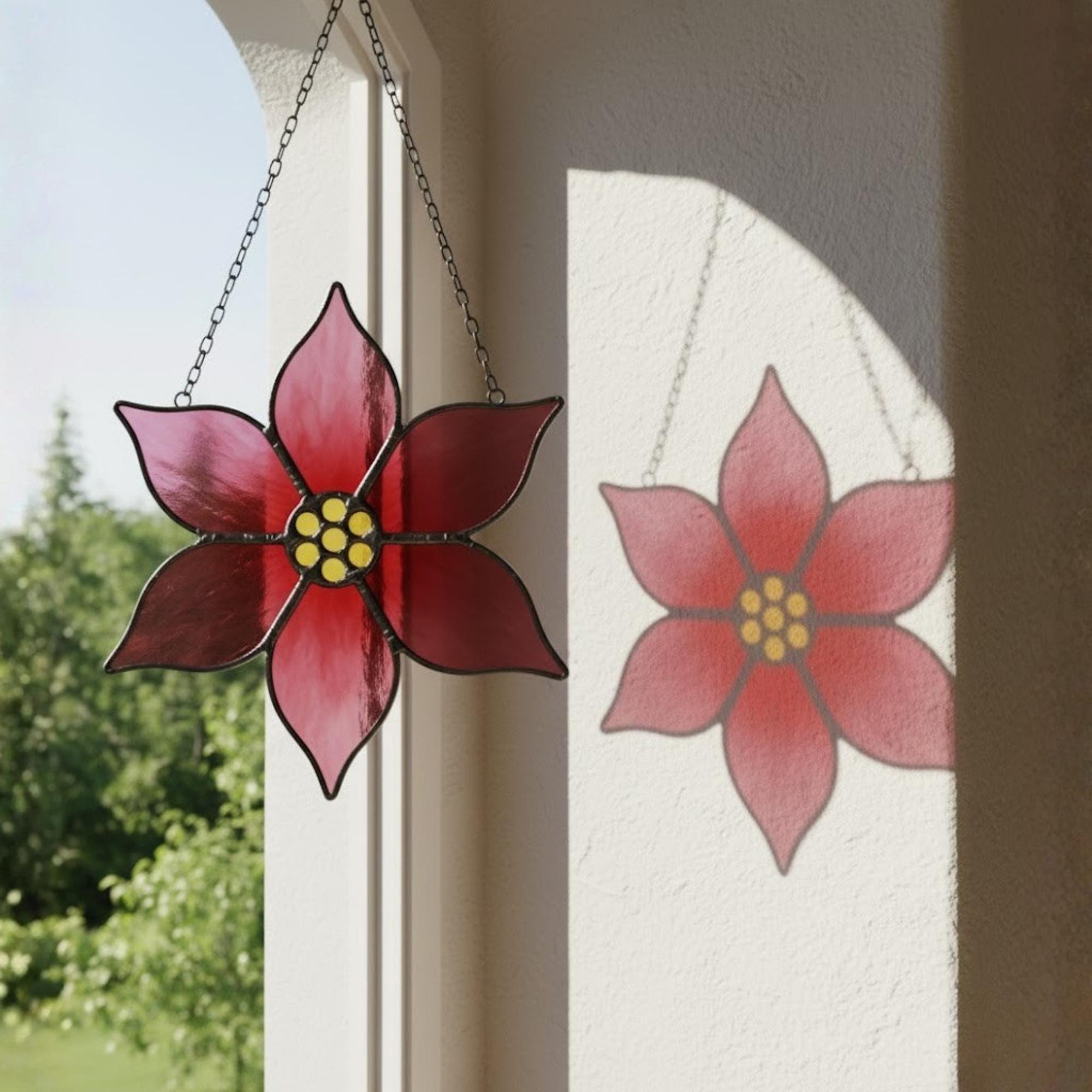 Two red glass poinsettia flowers hanging together as Christmas window decor.