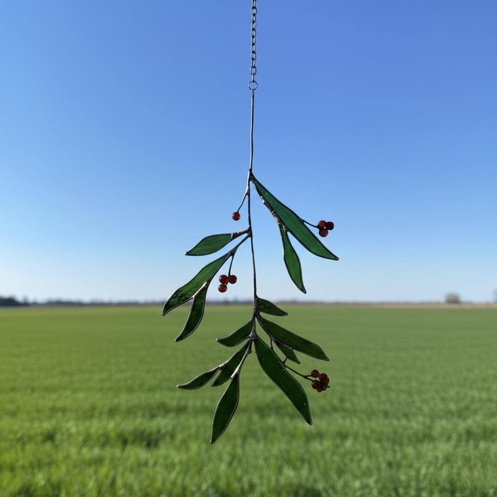 Woman’s hand holding handmade stained glass leaf ornament against blue sky.