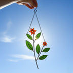 Red and green stained glass Christmas ornament glowing in sunlight.