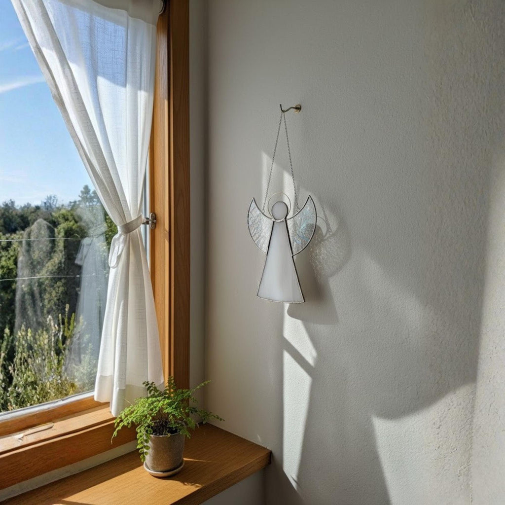 Angel stained glass ornament hanging on Christmas tree surrounded by twinkling holiday lights.