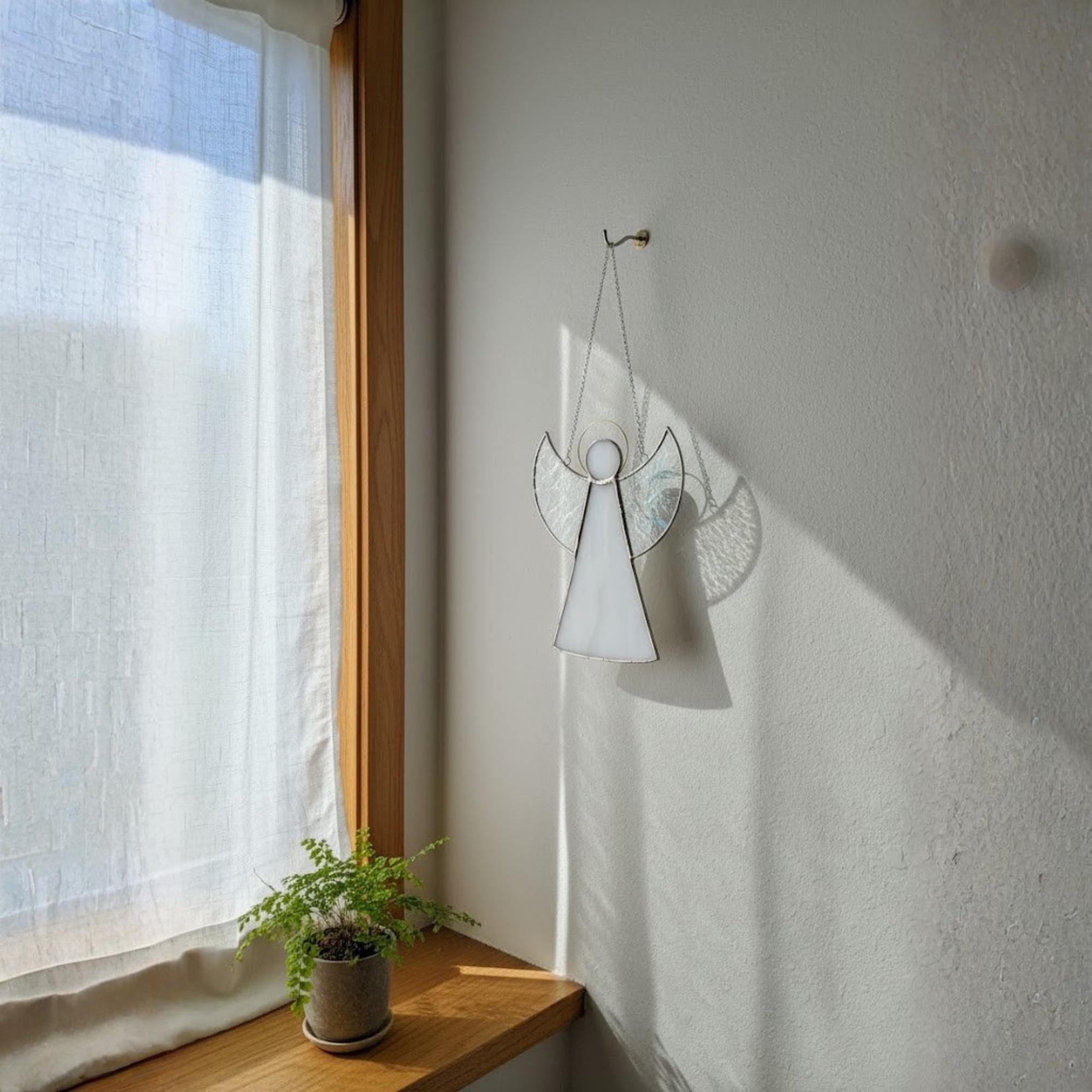 Handmade guardian angel stained glass hanging outside wall reflecting sunlight.