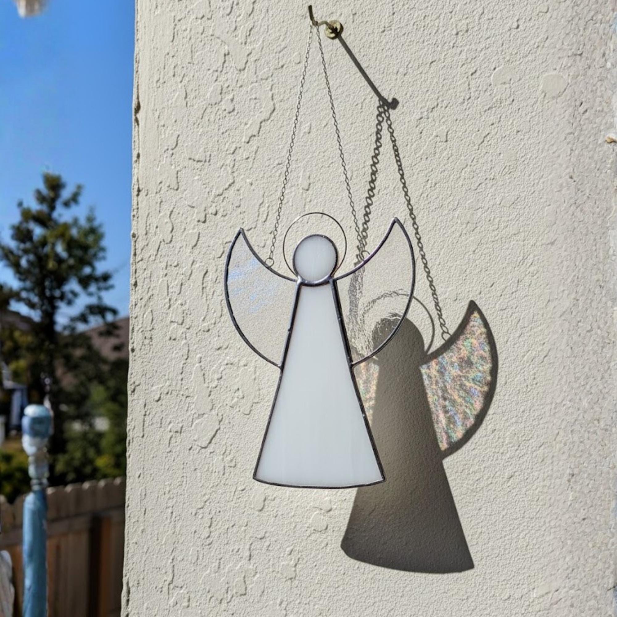Handmade stained glass angel ornament hanging on window, catching sunlight beautifully in cozy home.