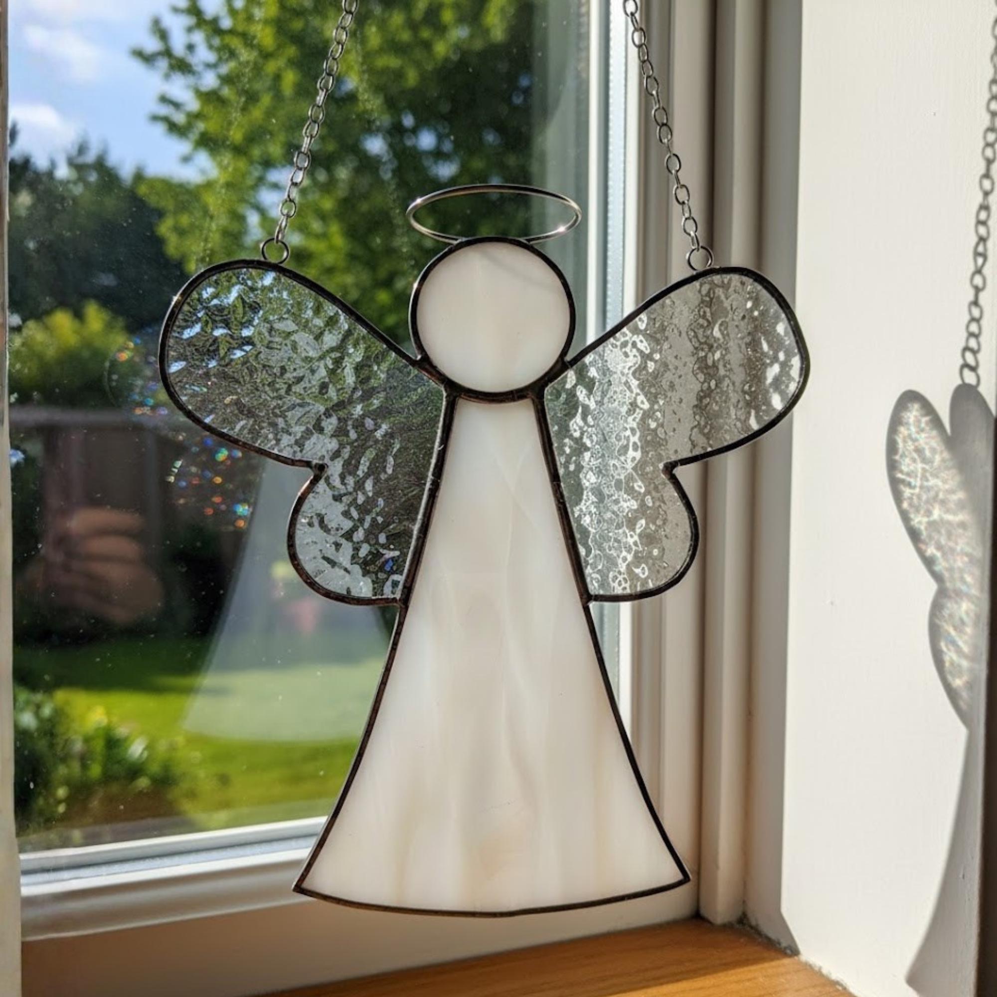 Clear glass angel ornament with halo detail reflecting rainbow light in bright room.