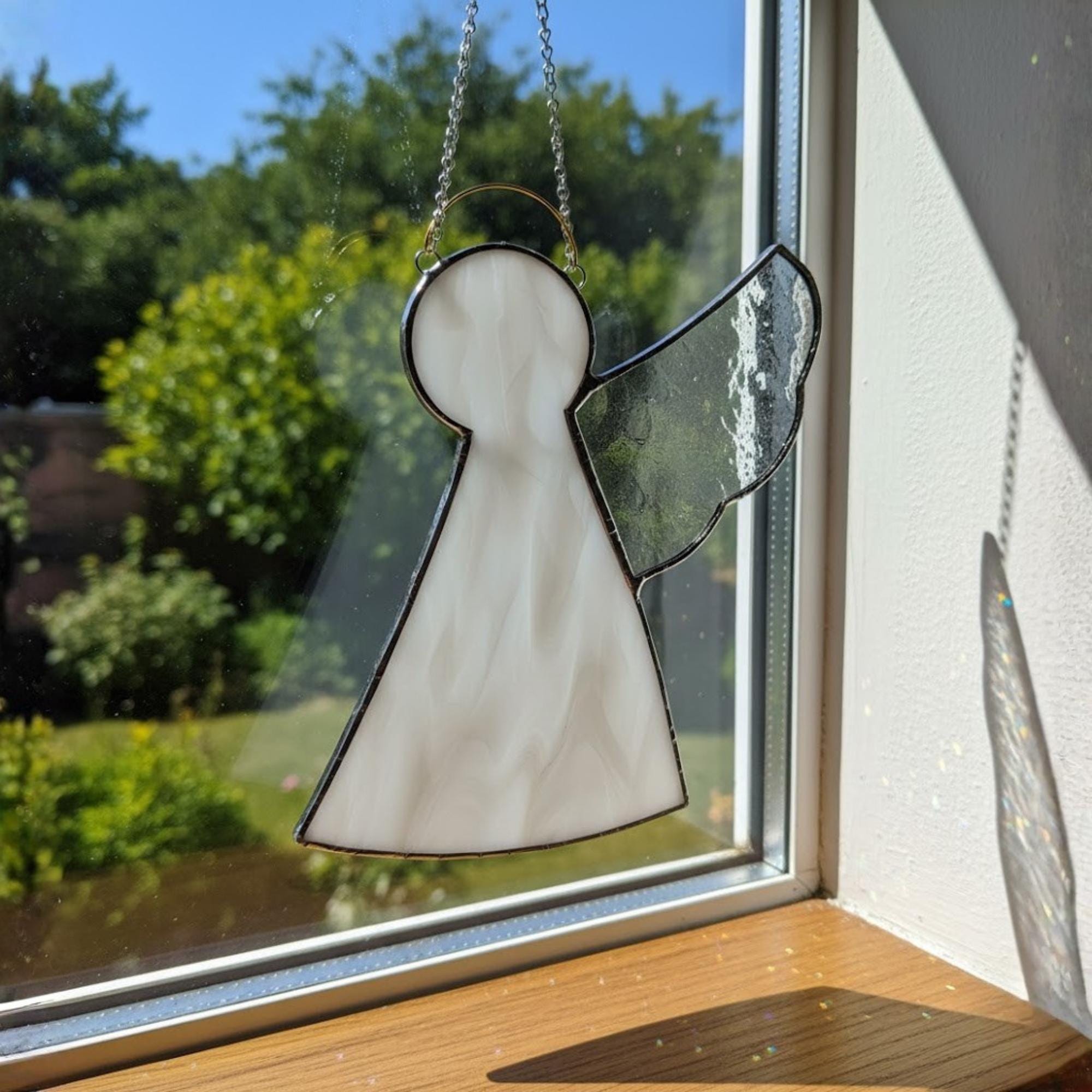 Stained glass angel ornament glowing in sunlight, symbol of faith and remembrance.