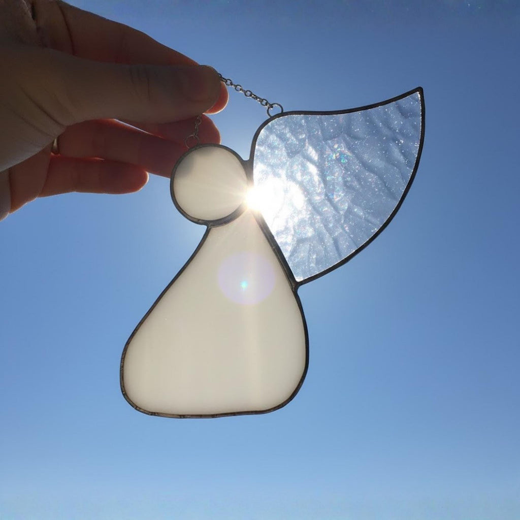 Woman decorating Christmas tree with handmade stained glass angel ornament.