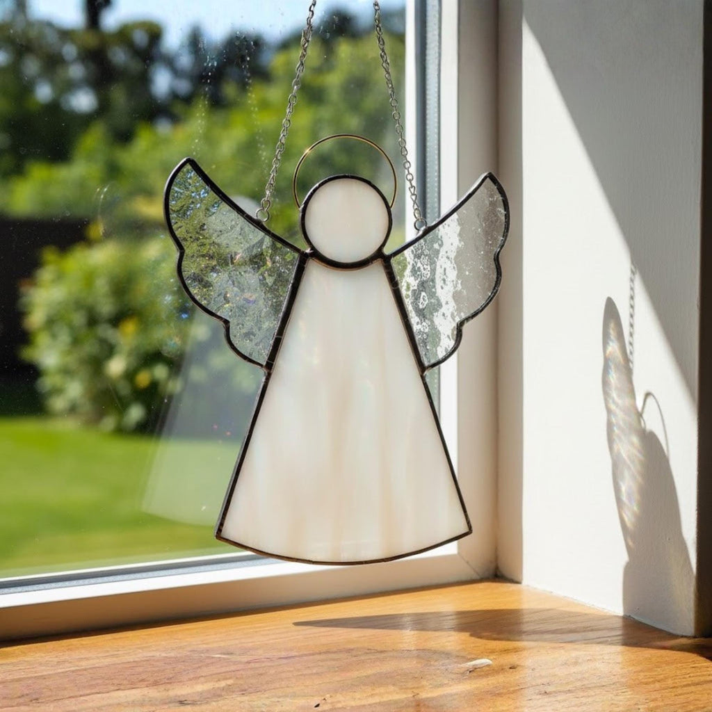 Handmade stained glass angel ornament catching sunlight through window for peaceful home decor.