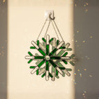 Green snowflake stained glass suncatcher glowing on wall, winter window decoration