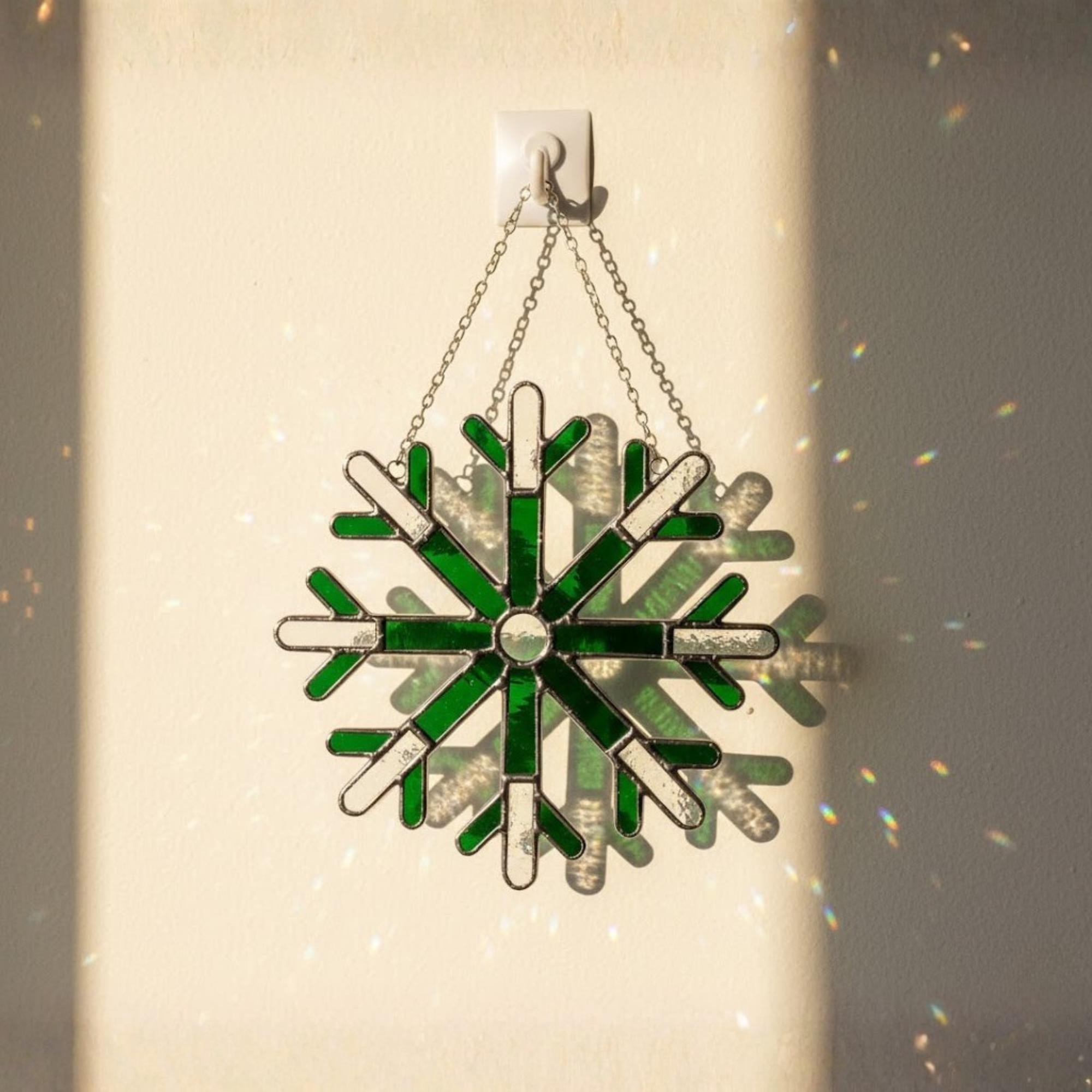 Green snowflake stained glass suncatcher glowing on wall, winter window decoration