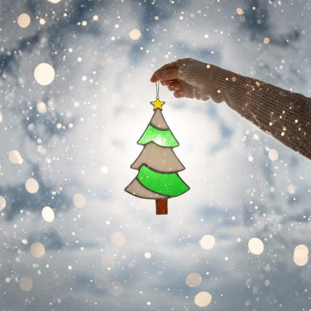 Stained glass Christmas tree ornament held in snowy scene, winter holiday photo