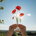 Single stained glass poppy stem held up to sunlight, handmade glass flower art