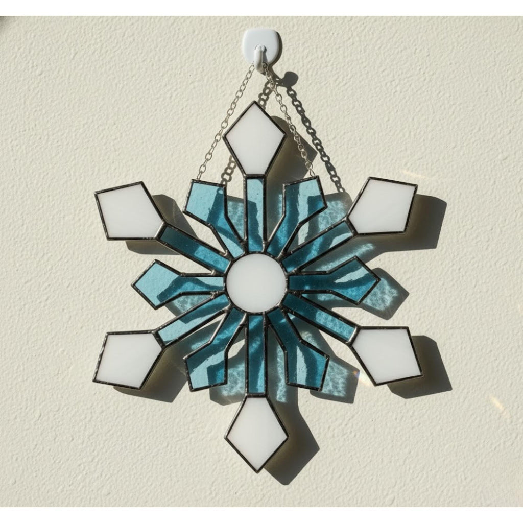 Detailed stained glass snowflake hanging on wall, icy blue winter decoration