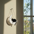 Cat-shaped stained glass moon ornament hanging by open window, soft natural light