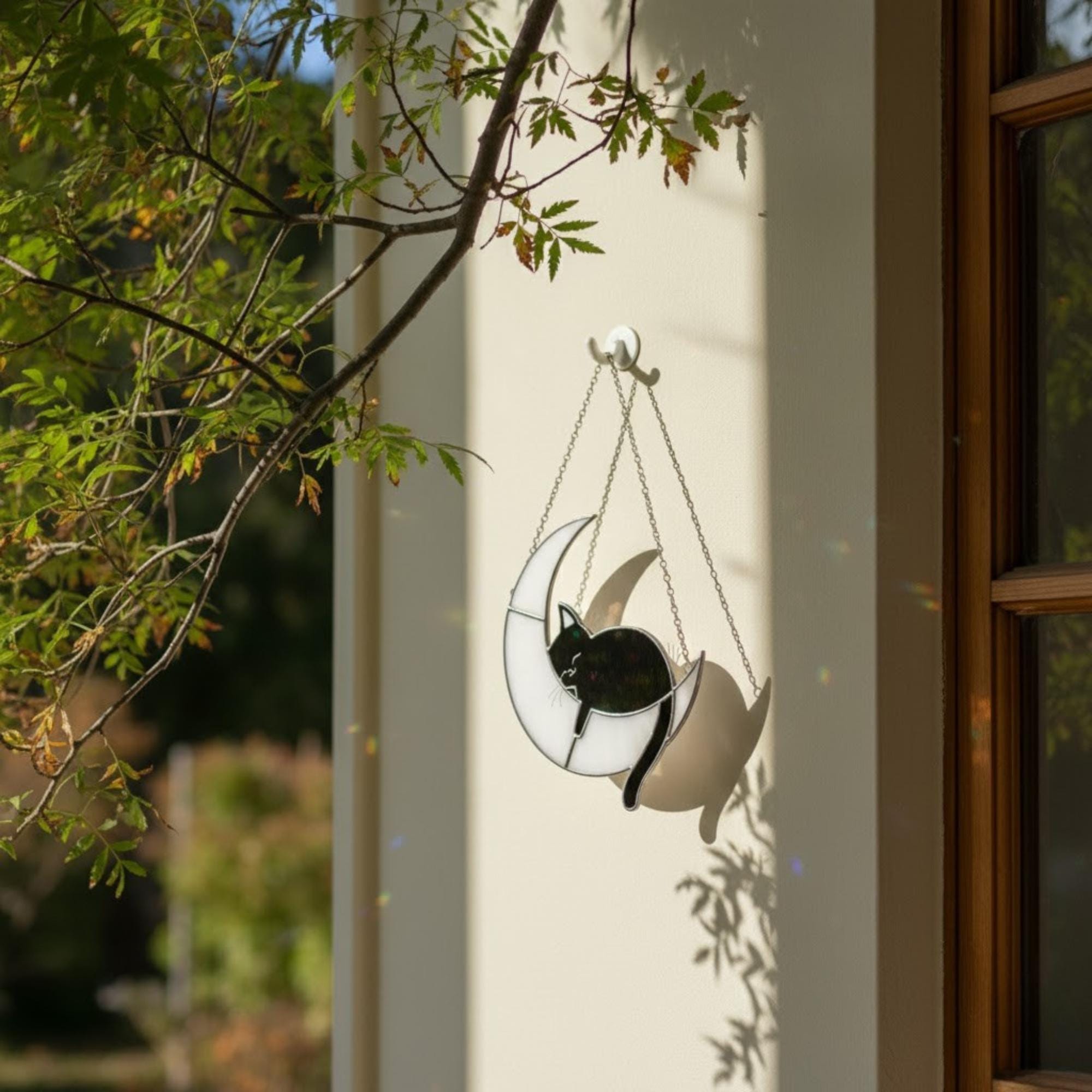 Moon cat ornament glowing in sunlight on window frame, handmade celestial art
