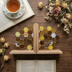 Handmade stained glass honeycomb bookends with metal bee detail, amber glass casting golden shadows, solid oak wood base for heavy books.