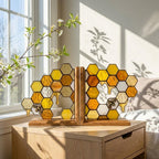 Handmade stained glass honeycomb bookends with metal bee detail, amber glass casting golden shadows, solid oak wood base for heavy books.