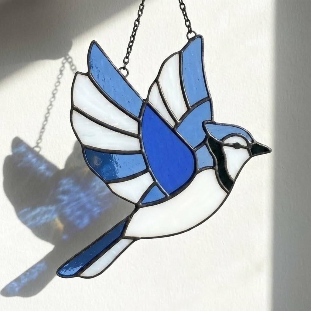 Stained glass Blue Jay bird suncatcher on branch hanging on window casting blue shadows, handmade realistic nature decor for birdwatchers by LuzyGlassArt.