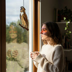Handmade stained glass owl suncatcher in brown and beige tones, perched on a branch, casting warm amber shadows on a white wall, Tiffany style soldering detail.