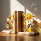 Handmade stained glass honeycomb bookends with metal bee detail, amber glass casting golden shadows, solid oak wood base for heavy books.