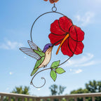 Handmade hummingbird and red hibiscus flower stained glass suncatcher casting vibrant colored shadows, perfect tropical botanical decor and memorial gift for mom.
