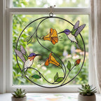 Handcrafted stained glass hummingbird and floral suncatchers in a circular metal hoop, casting colored shadows, packaged in a luxury wooden gift box for Mother's Day.