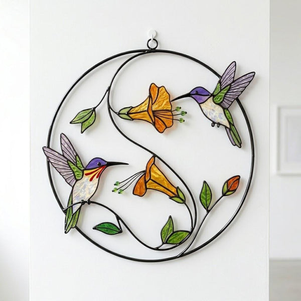 Handcrafted stained glass hummingbird and floral suncatchers in a circular metal hoop, casting colored shadows, packaged in a luxury wooden gift box for Mother's Day.
