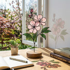 Handcrafted 3D stained glass pink cherry blossom sakura flower standing on a solid wooden base casting colored shadows on a desk, perfect Mother's Day gift.
