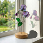 Handcrafted 3D stained glass purple sweet pea flower standing on a solid wooden base casting colored shadows, perfect April birth flower or Mother's Day desk decor gift.
