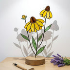 Handcrafted stained glass coneflower black eyed susan family bouquet standing on a custom personalized engraved wooden base casting colored shadows, perfect Mom's garden Mother's Day desk decor gift.