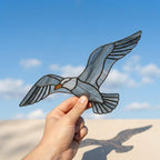 Handcrafted wispy stained glass flying seagull suncatcher casting shadows, perfect coastal beach house decor and nautical ocean lover gift.