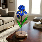 Handcrafted 3D stained glass blue iris flower standing on a wooden base with a brass nameplate, casting colored shadows, perfect Mother's Day desk decor gift.
