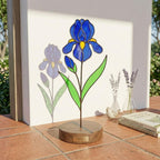 Handcrafted 3D stained glass blue iris flower standing on a wooden base with a brass nameplate, casting colored shadows, perfect Mother's Day desk decor gift.