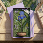 Handcrafted 3D stained glass blue iris flower standing on a wooden base with a brass nameplate, casting colored shadows, perfect Mother's Day desk decor gift.