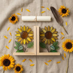 Yellow stained glass sunflower bookends with green leaves on a natural wood base holding books, catching spring sunlight on a desk.